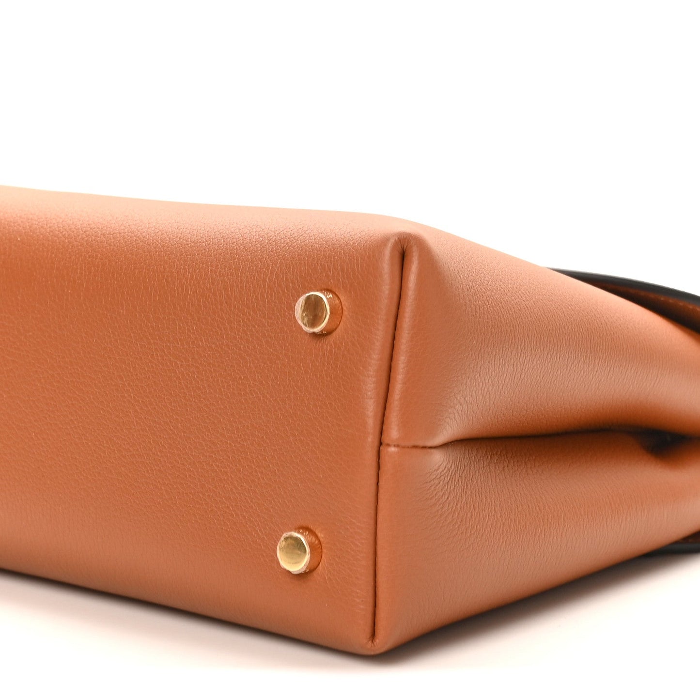 Tan leather handbag corner close-up with two gold snap buttons and curved base edge