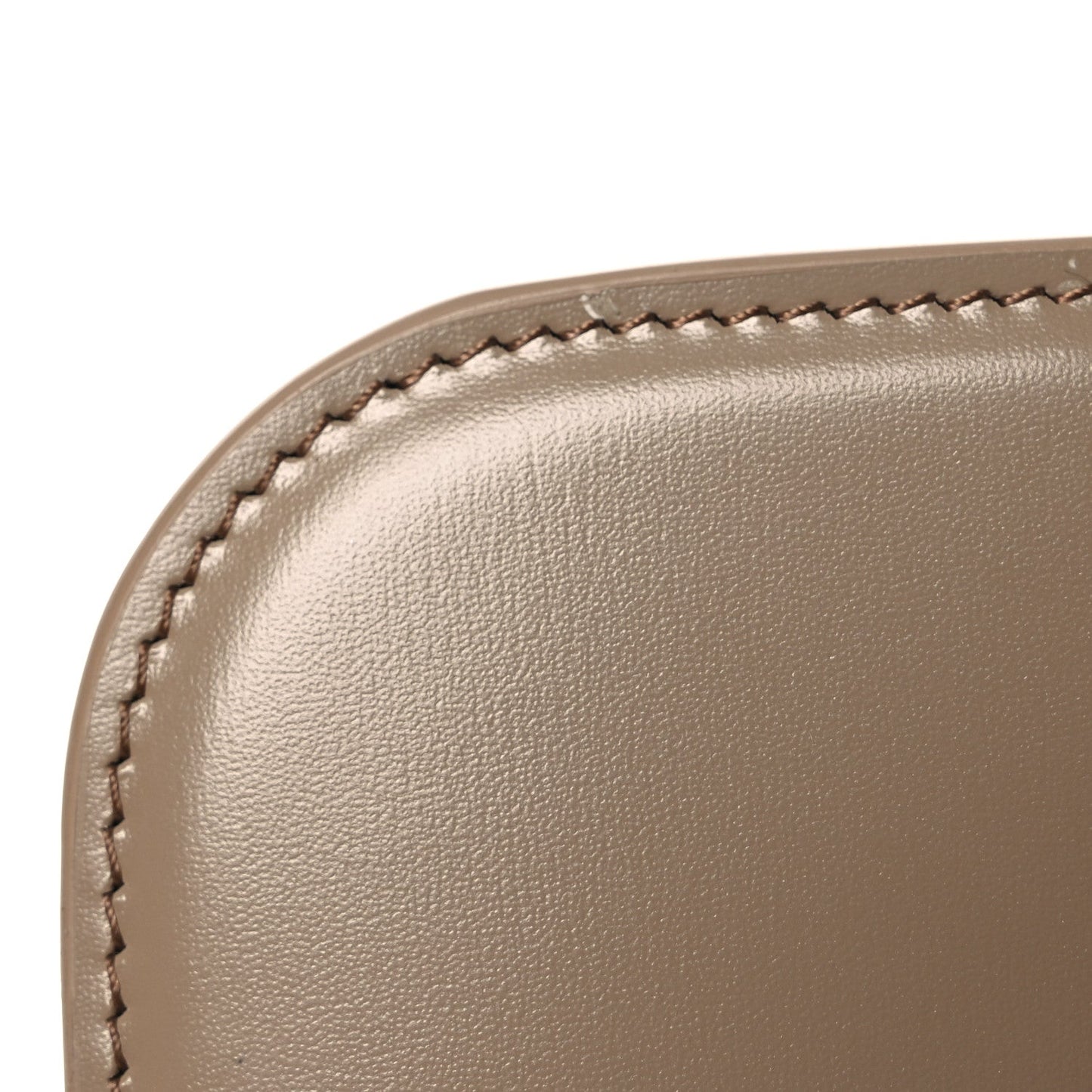 Shiny brown leather bag corner close-up with stitched edge and smooth grain