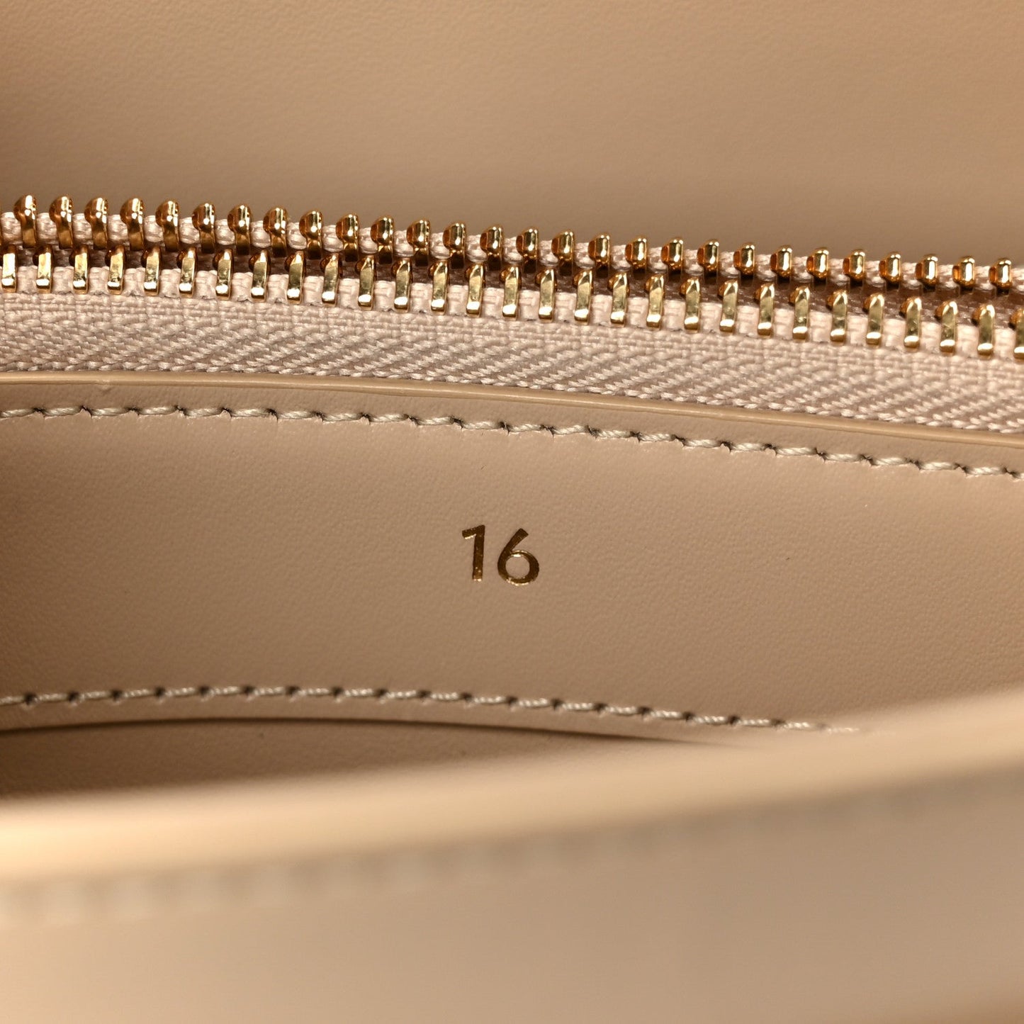 Gold zipper teeth and beige lining with stitched seam inside a small bag