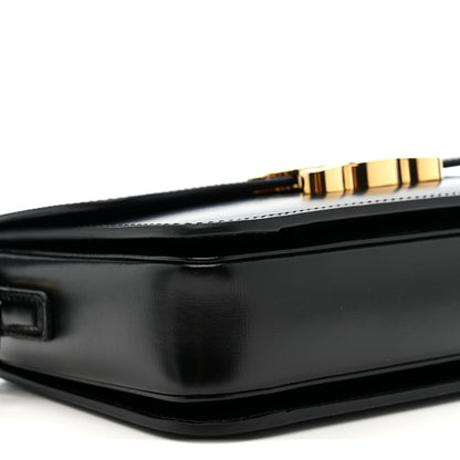 Black leather crossbody bag side with gold-tone clasp detail and smooth structured shape.