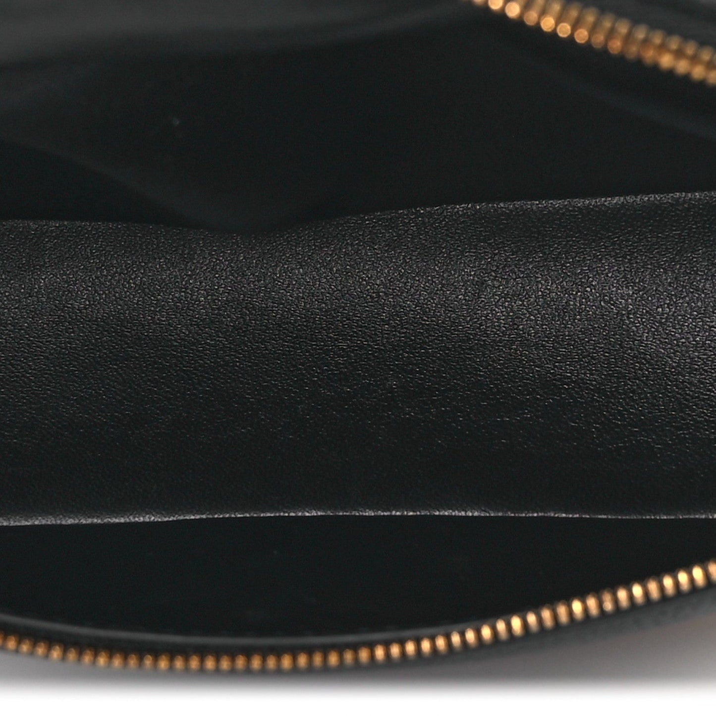 Black grained leather close-up with gold-tone zipper teeth along the opening