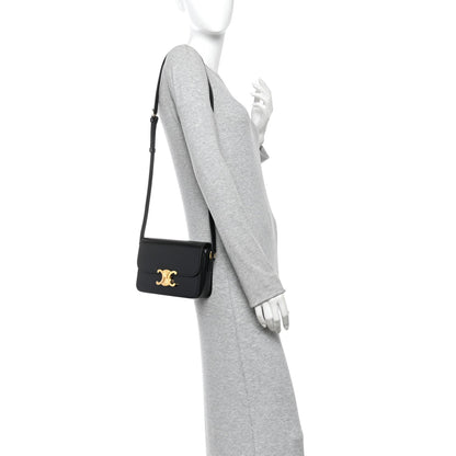 Black mini shoulder bag on model with gold logo, worn crossbody with slim strap.