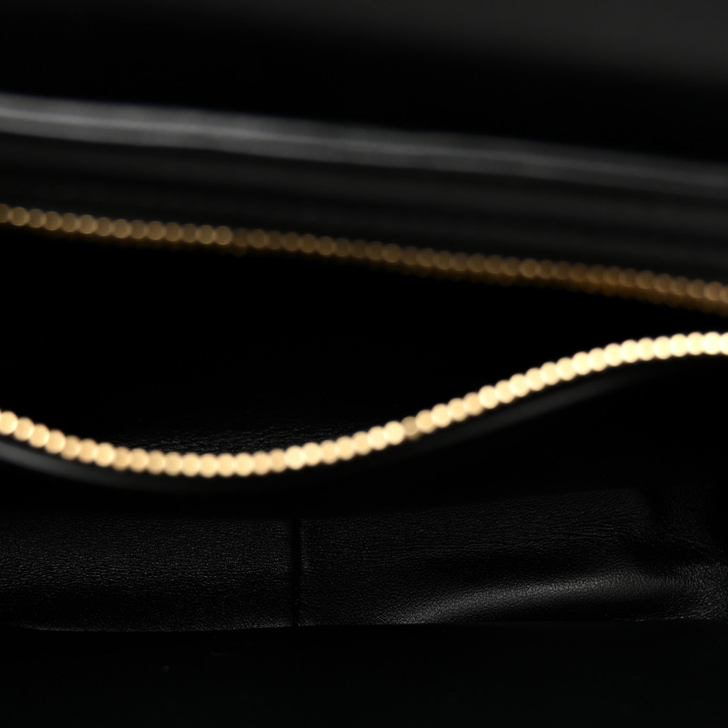 Close-up of black leather bag interior edge with gold chain trim.