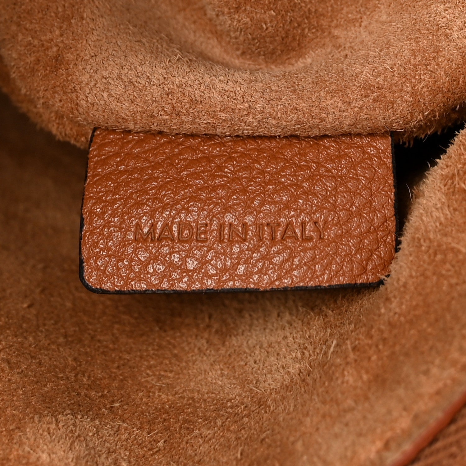 Tan leather interior pocket label with embossed text on a small hobo bag