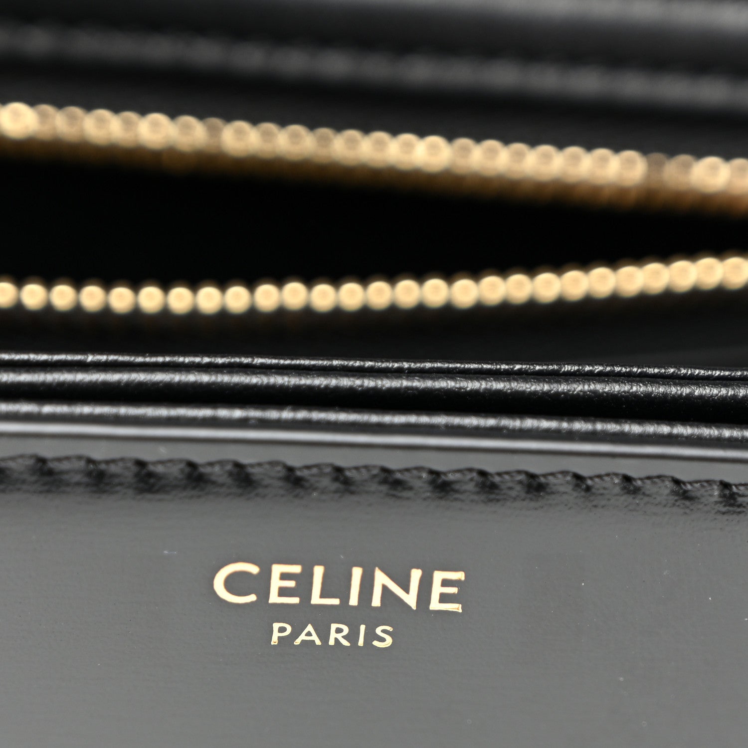 Close-up of black leather bag stitching and gold chain detail.