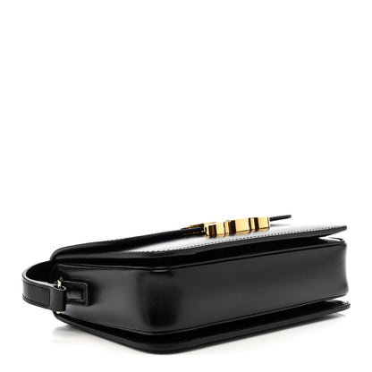 Black leather crossbody bag with gold buckle and structured base, side view.