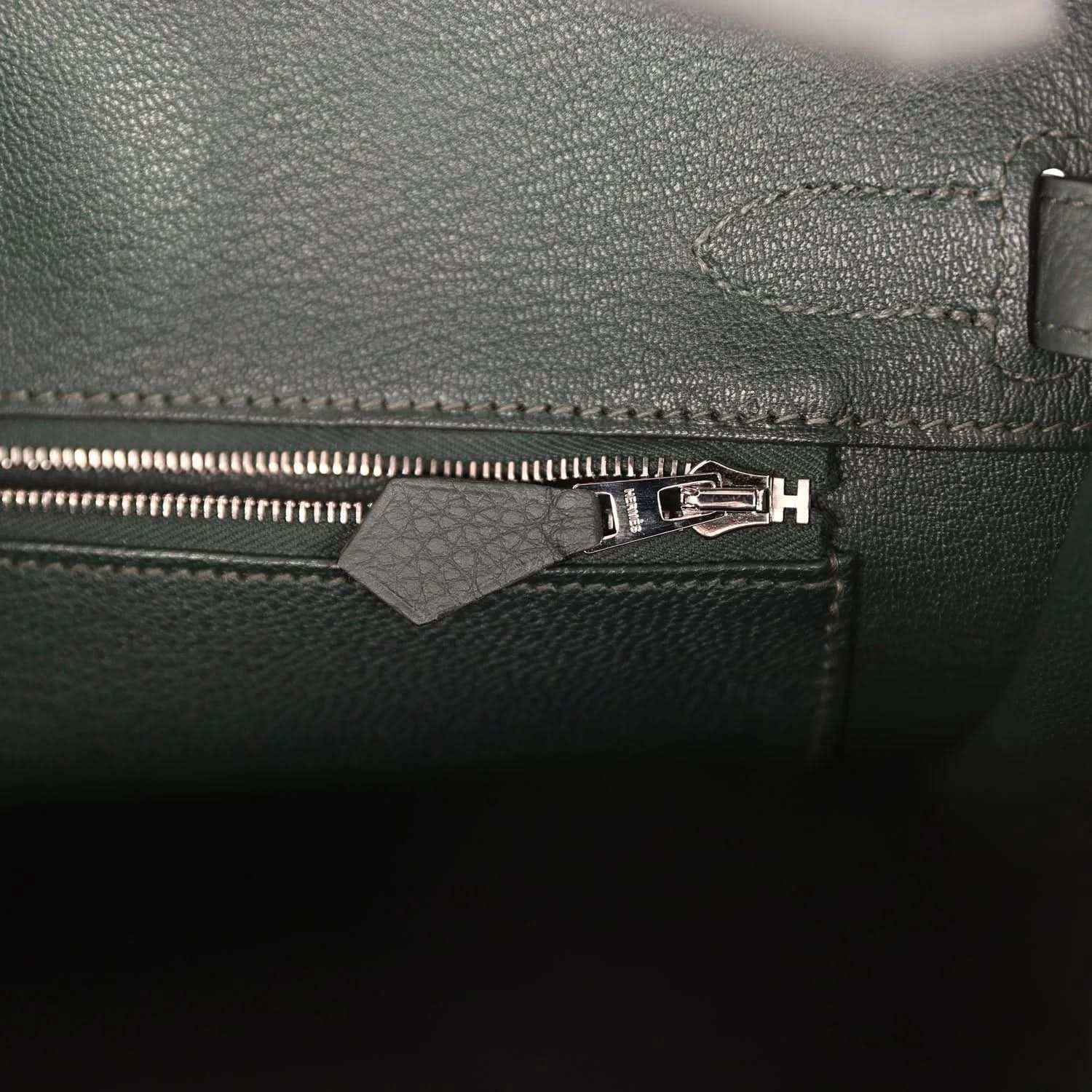 Sophisticated dark green leather handbag with elegant silver zipper detailing.