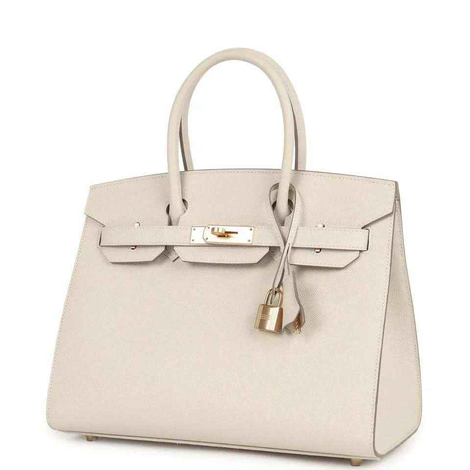 Top-handle leather handbag with front flap, gold-toned clasp and lock, light neutral.