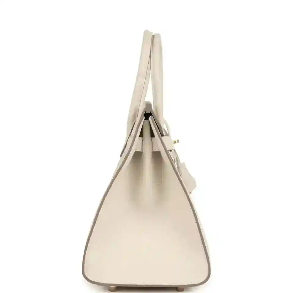 Top-handle leather handbag with gold-toned hardware, tapered shape, light neutral.