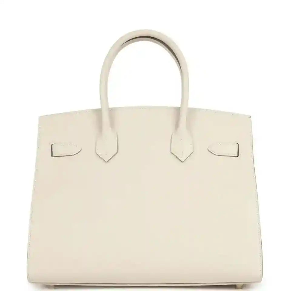 Top-handle leather handbag with two handles and back flap detail, light neutral.
