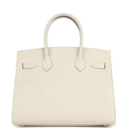 Top-handle leather handbag with two handles and back flap detail, light neutral.