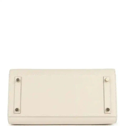 Leather handbag rear panel with metal hardware and studs, light neutral.