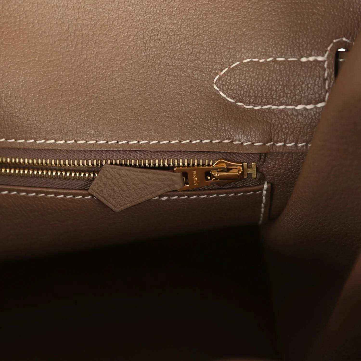 Elegant taupe leather handbag interior with gold zipper and white stitching, timeless style