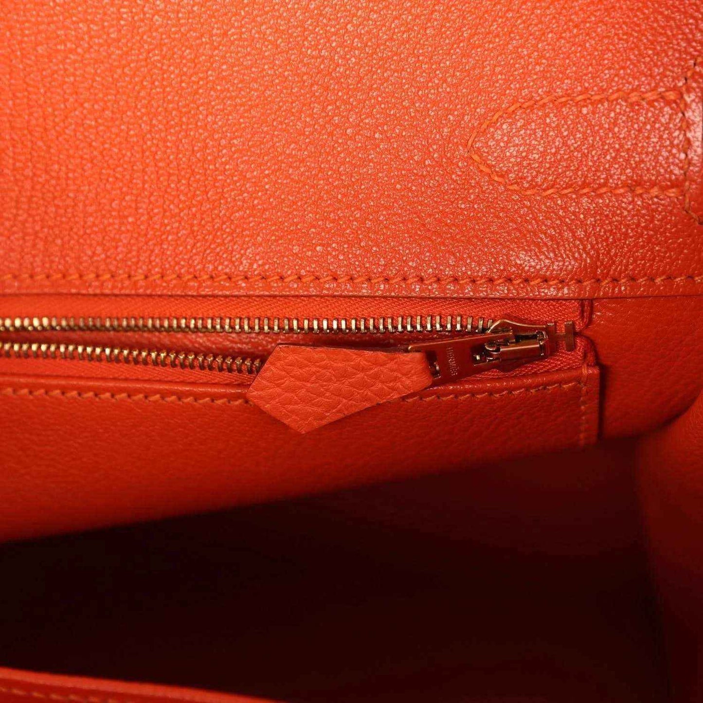 Elegant orange leather handbag interior with a gold zipper, showcasing timeless sophistication.