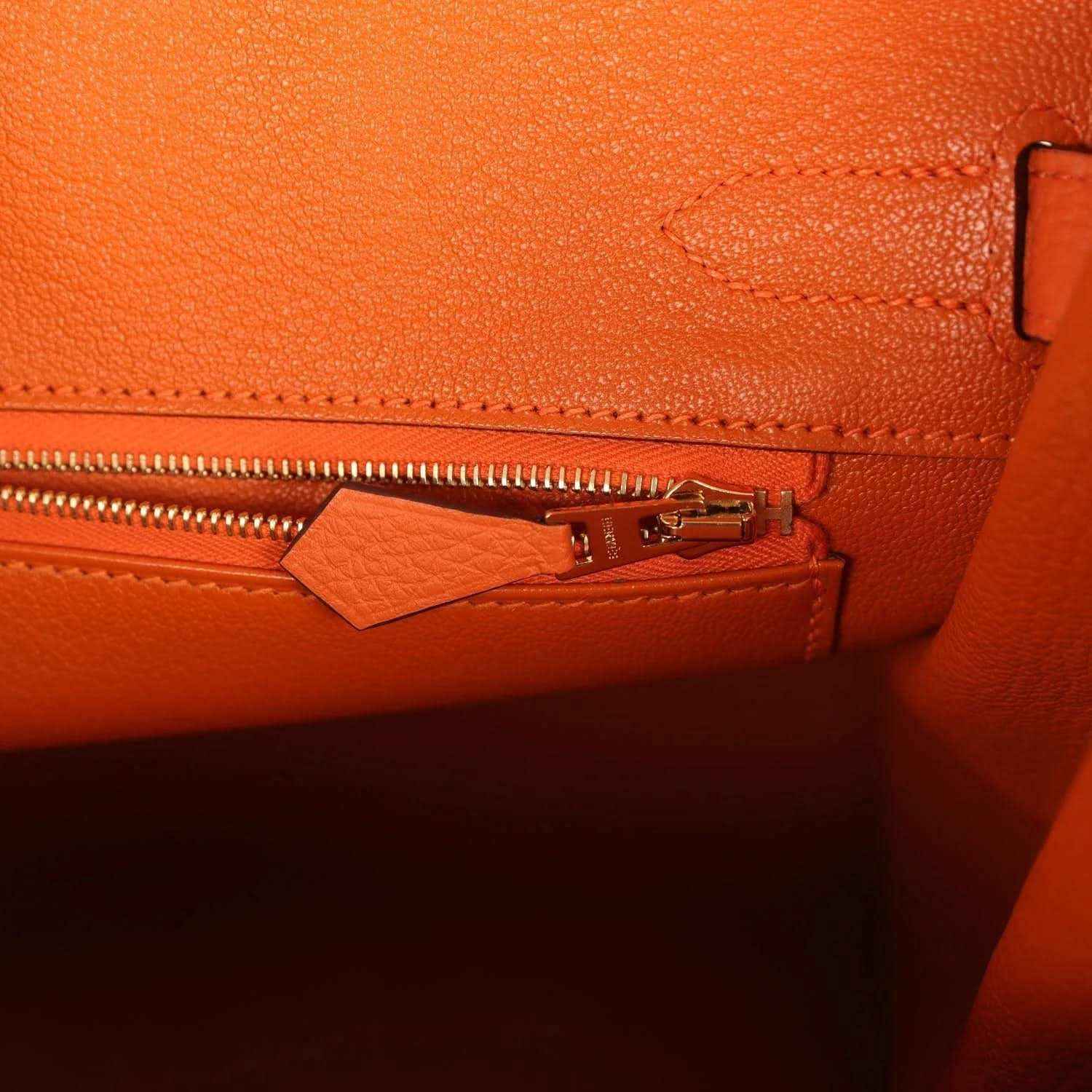 Elegant orange leather handbag interior with gold zipper detail, featuring refined stitching.