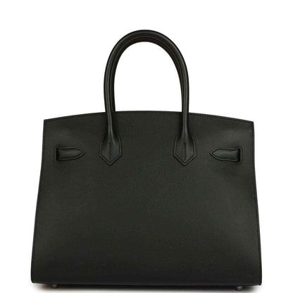 Black leather handbag with structured body, top handles, and front patch details