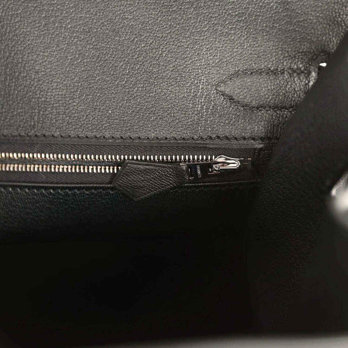 Black leather handbag interior close-up with zipper pull and reinforced seam