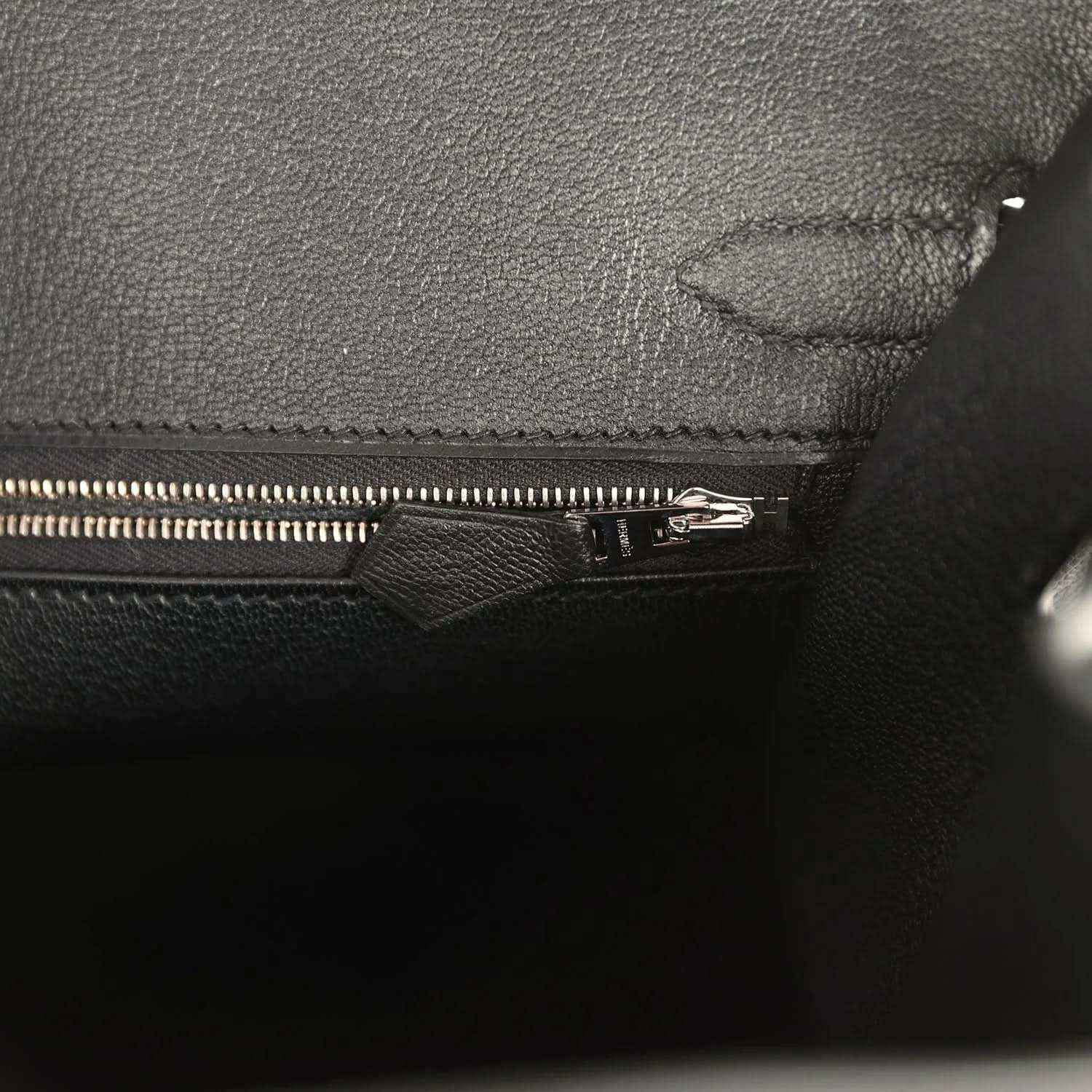 Black leather handbag interior close-up with zipper pull and reinforced seam