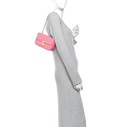 Flamingo pink mini leather shoulder bag with gold chain, held on an arm
