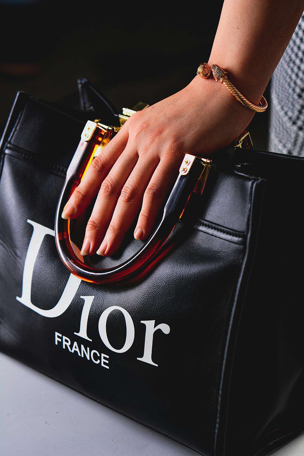 Black Dior handbag with a hand holding a glass of wine against a dark background
