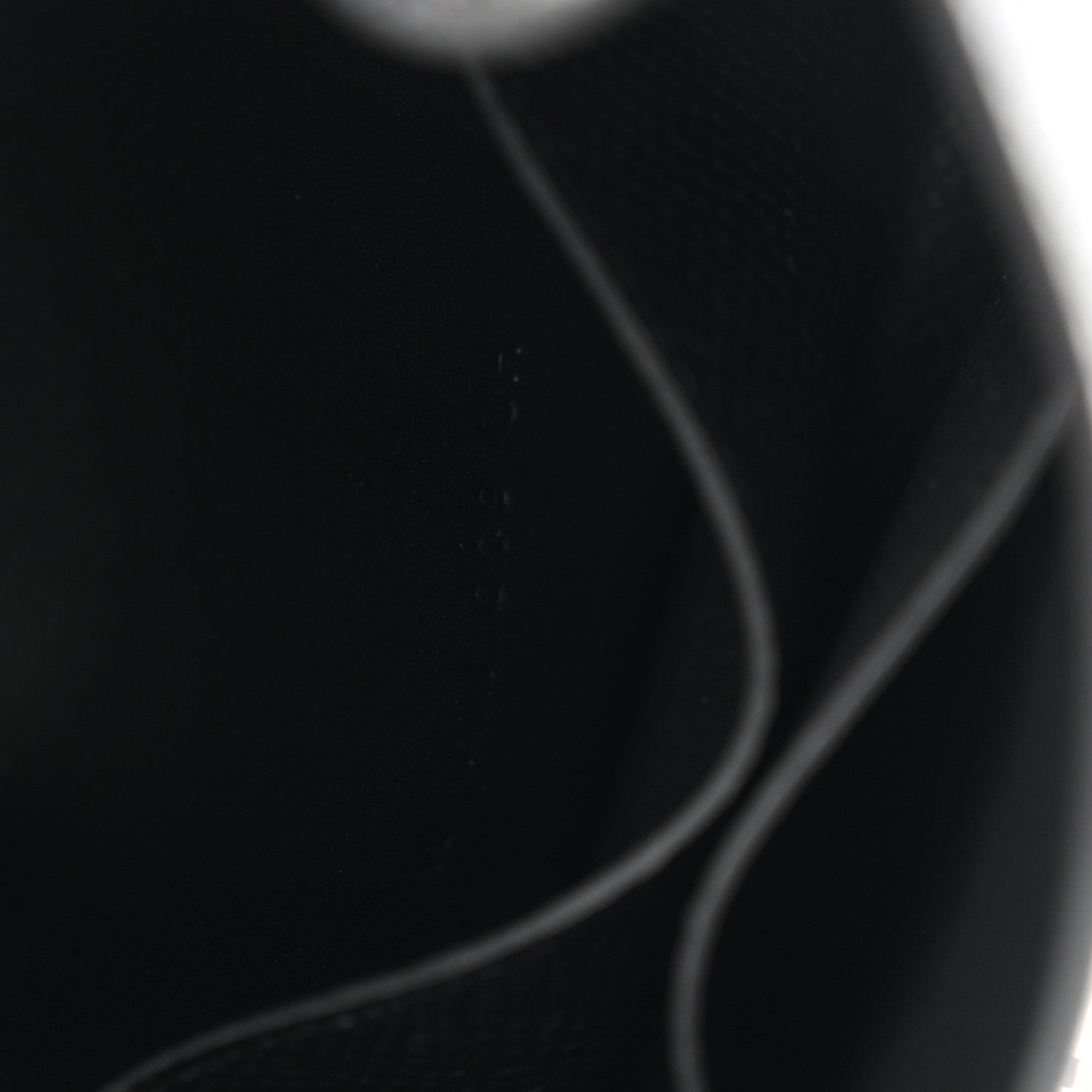 Black leather wallet corner with curved seam and edge stitching.