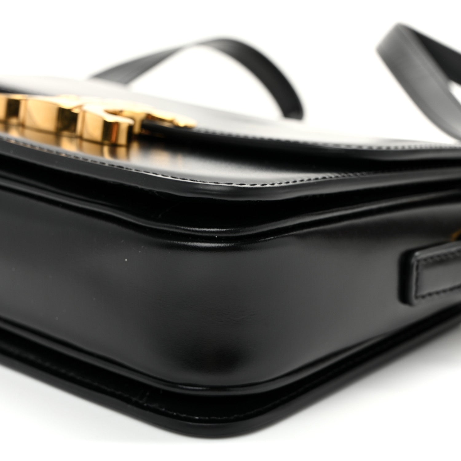 Close-up of black flap seam, white topstitching, and gold-tone hardware on strap.