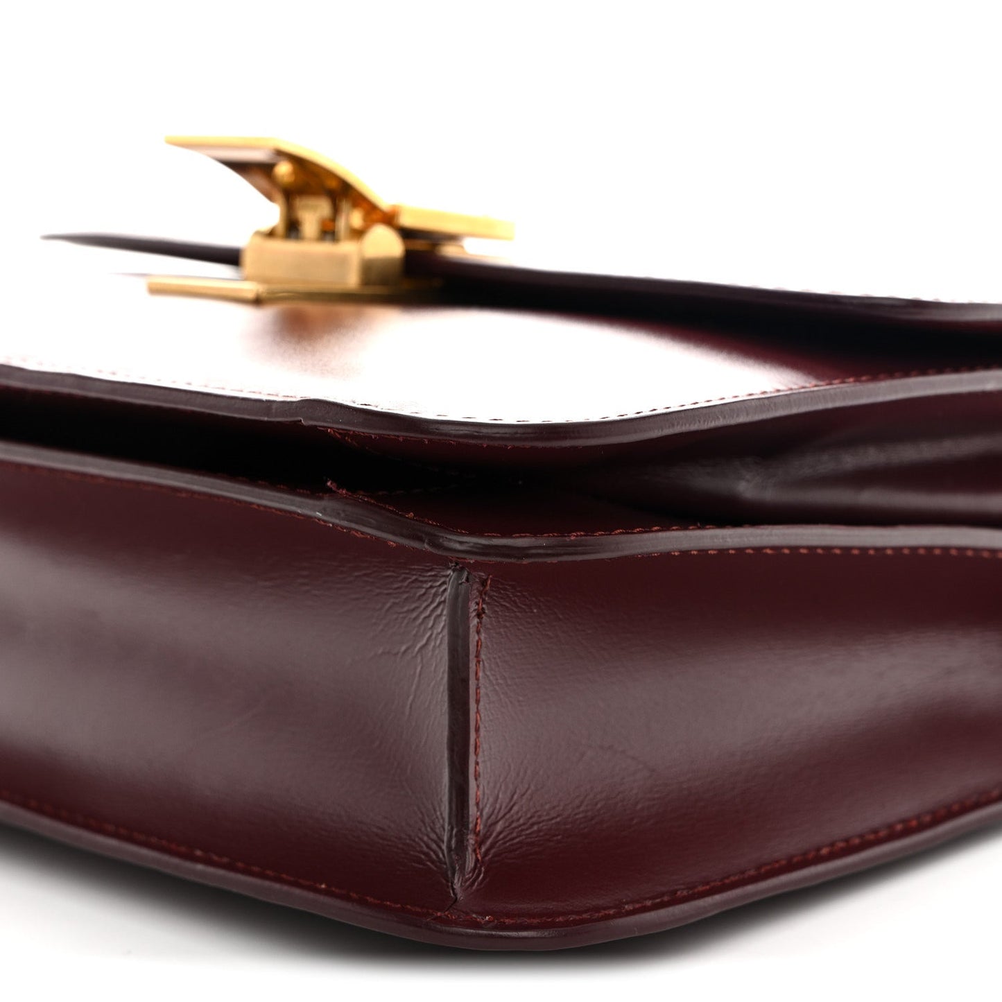 Burgundy leather bag side with gold-tone clasp and glossy corner seam detail.