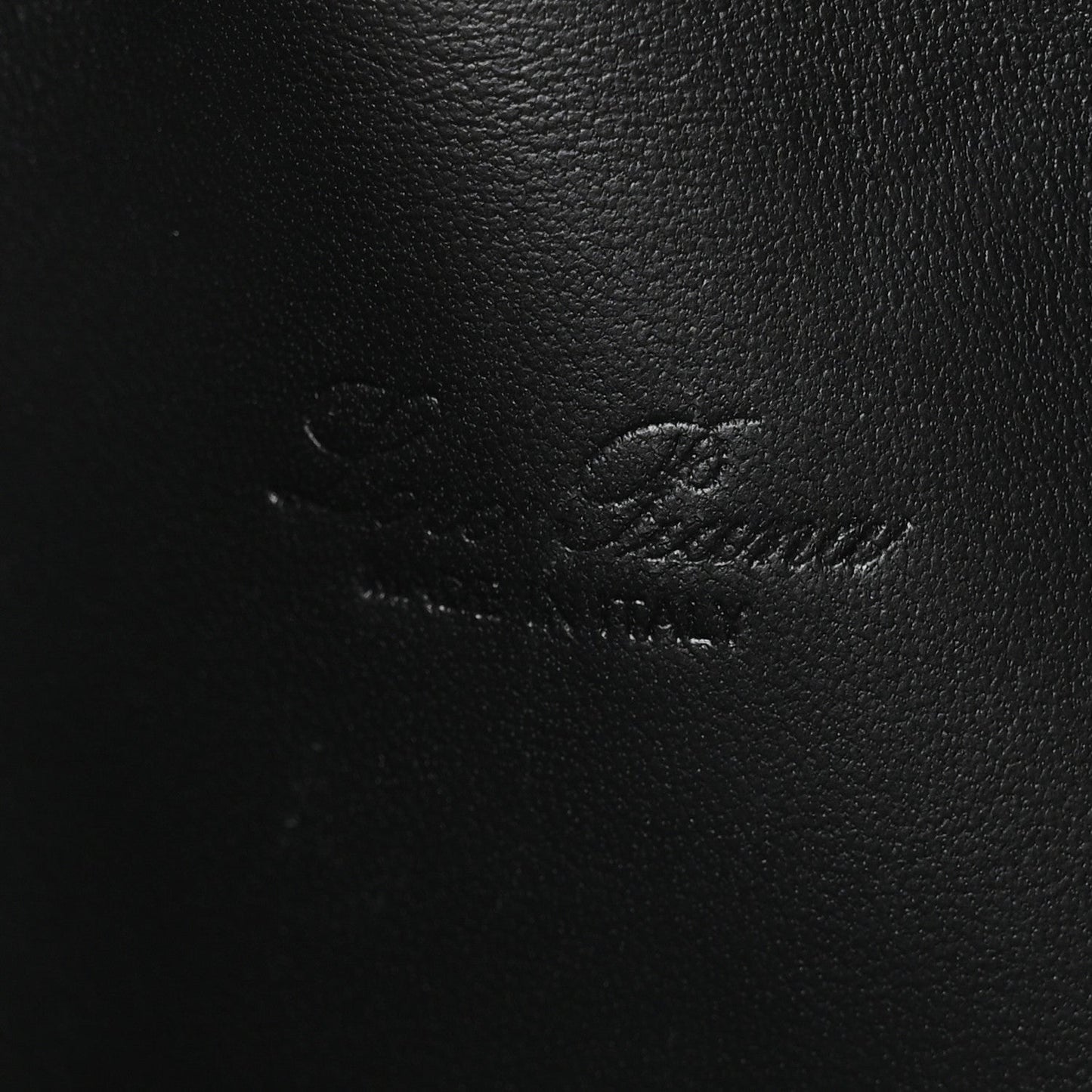 Close-up of black ostrich-textured leather pouch surface with subtle stitching