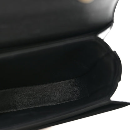 Black shiny mini crossbody bag, close-up of leather texture and curved front