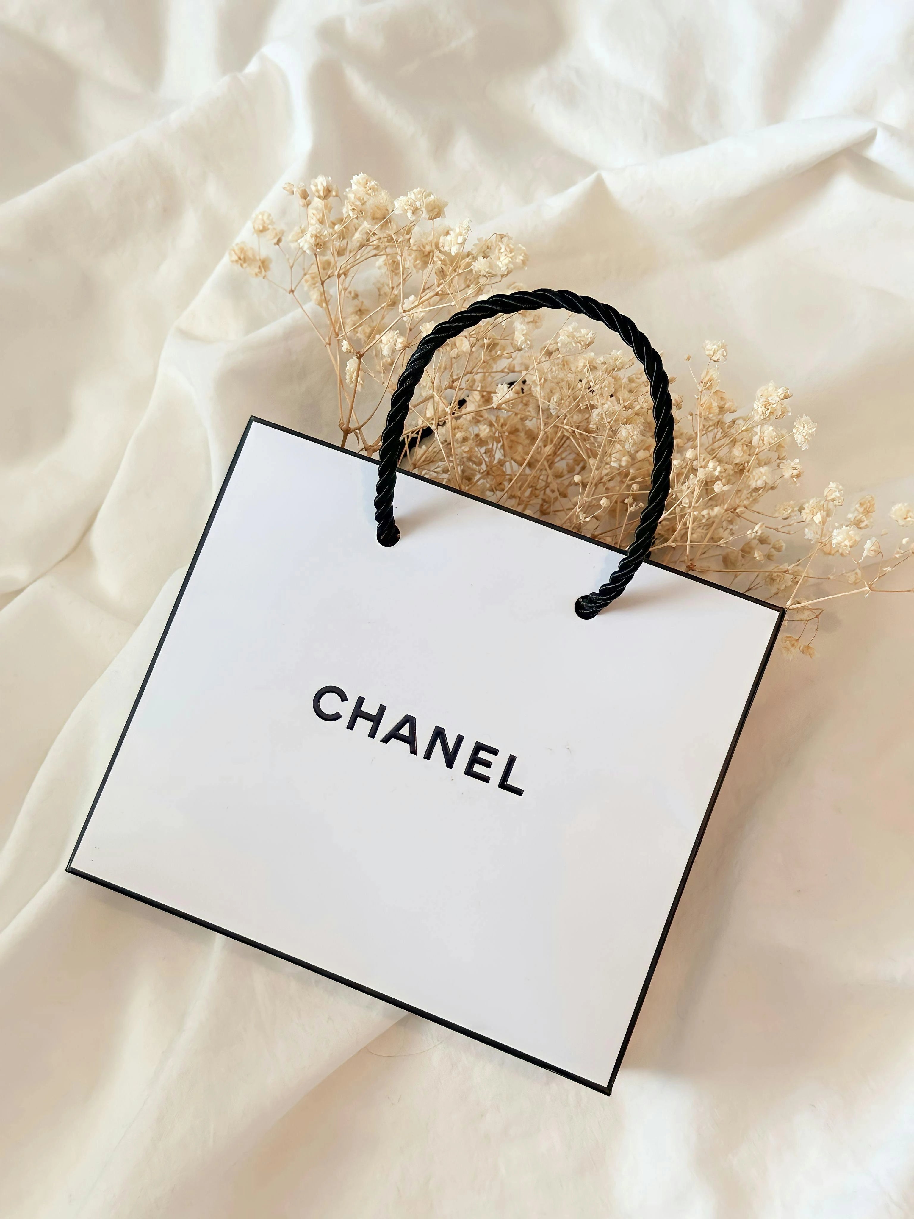 Chanel shopping bag with dried flowers on a soft beige fabric background