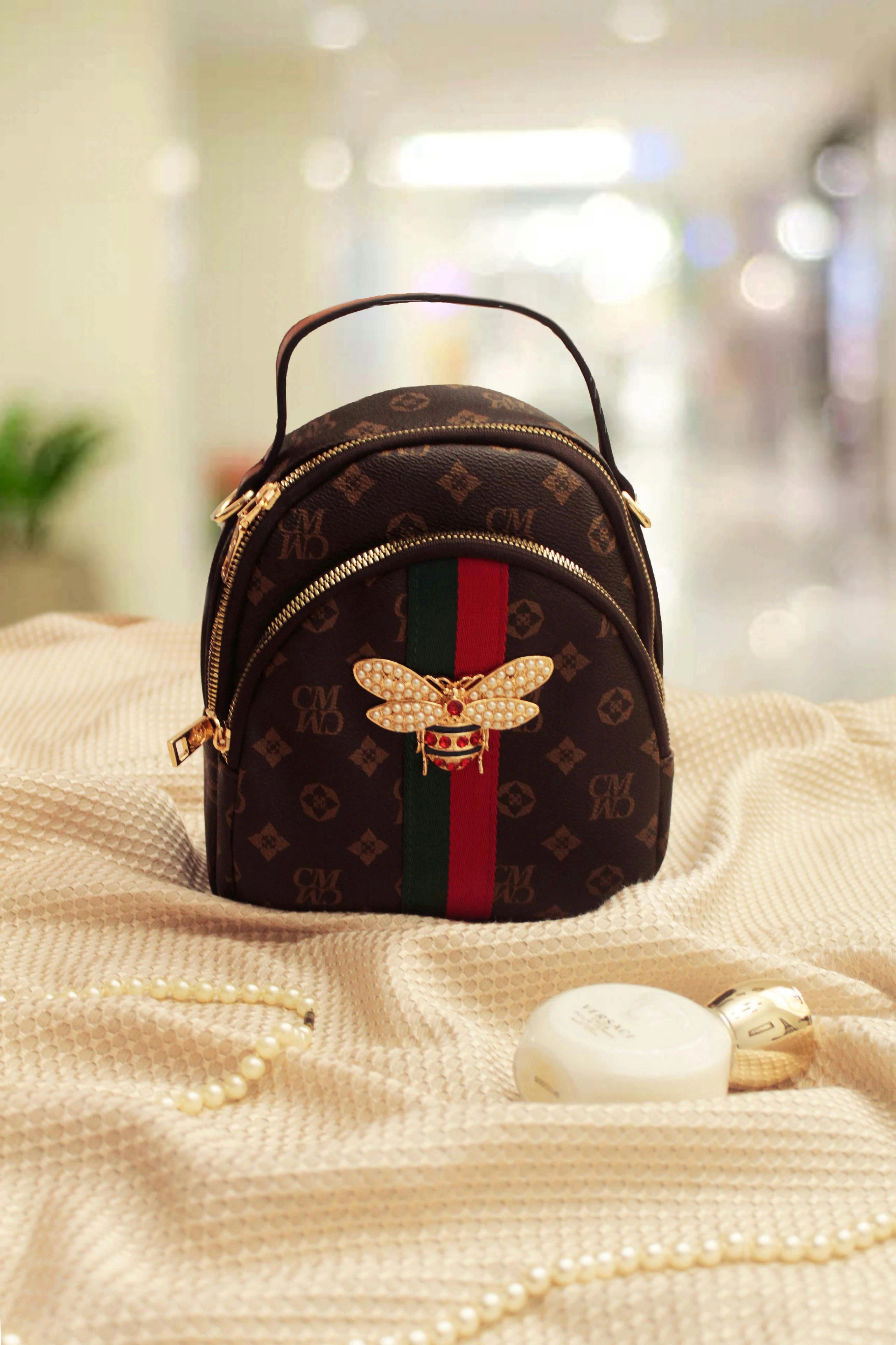 Designer handbag with bee emblem and colorful stripe on a textured surface