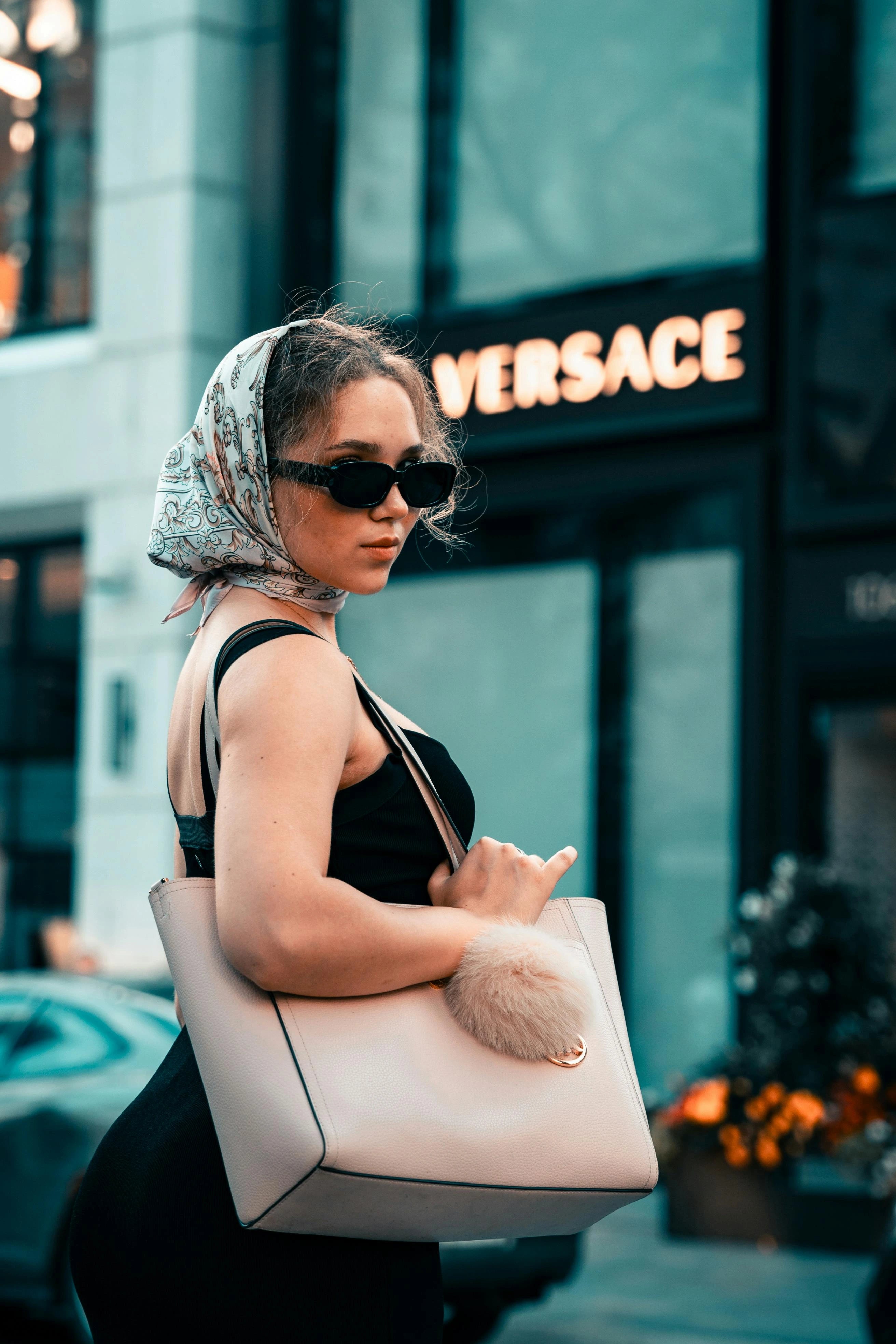 Woman holding a beige handbag with a fur pom-pom in front of a Versace store sign.