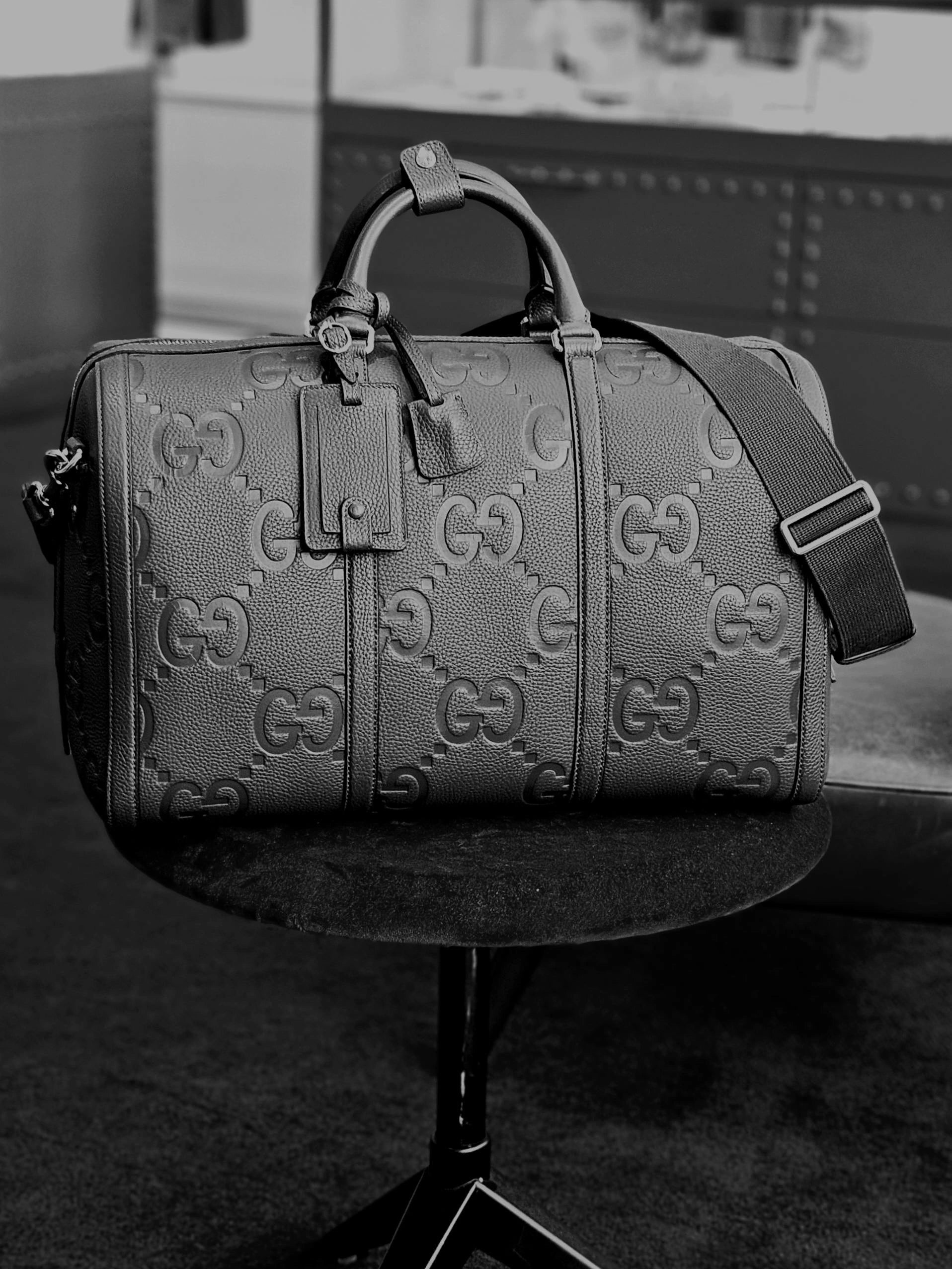 Gray duffel bag with Gucci logo on a black stand