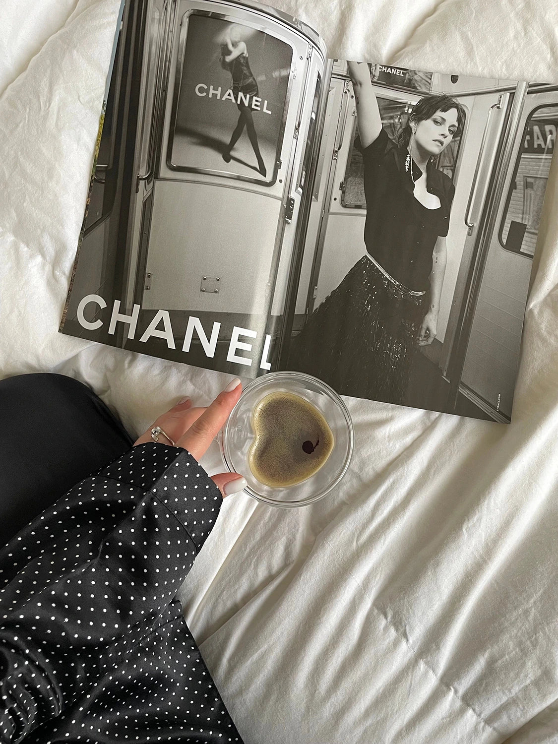 Open magazine with Chanel branding on a white surface, accompanied by a heart-shaped coffee cup.