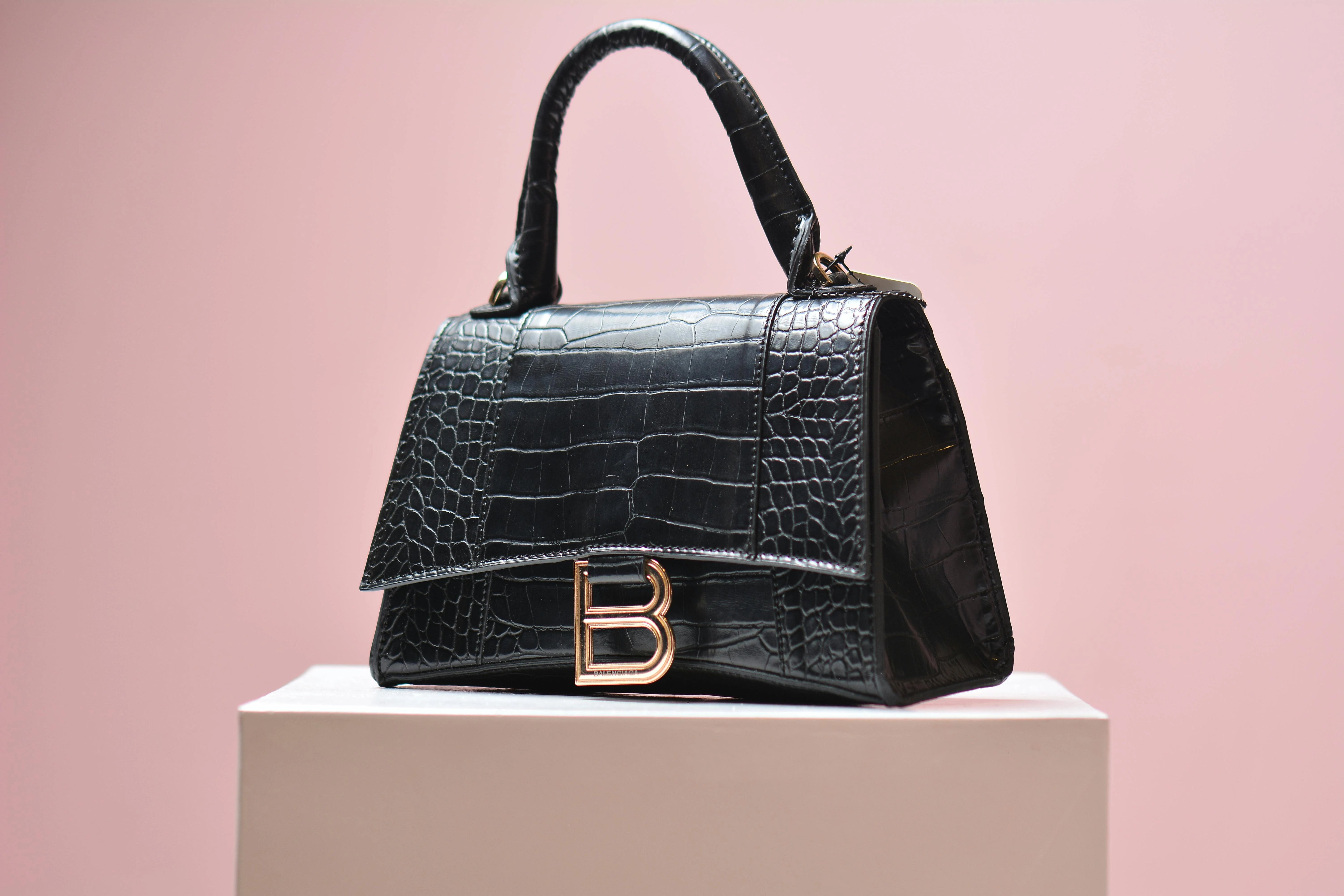 Black crocodile-patterned handbag with a gold logo on a pink background